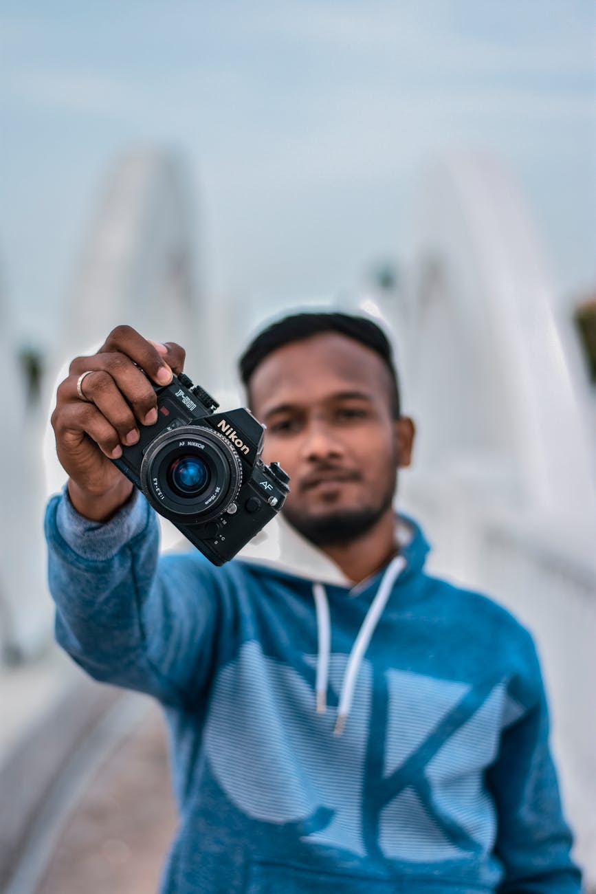 Close-up of a man holding a camera with a blurred background, emphasizing photography.