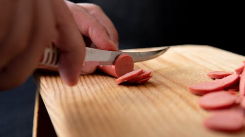 Crop cook cutting tasty sausage with knife in kitchen