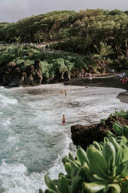 A picturesque view of the black sand beach in Hana, Hawaii, surrounded by lush greenery and ocean waves.