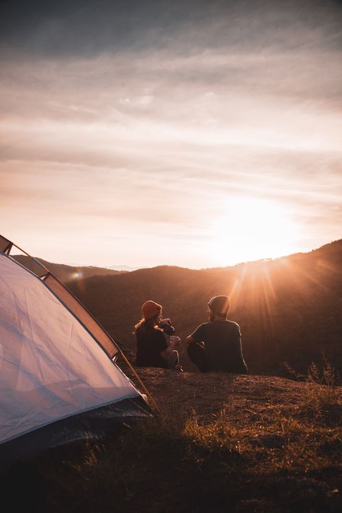 Free A couple sits by their tent, overlooking a scenic sunset in Garopaba, Brazil. Stock Photo