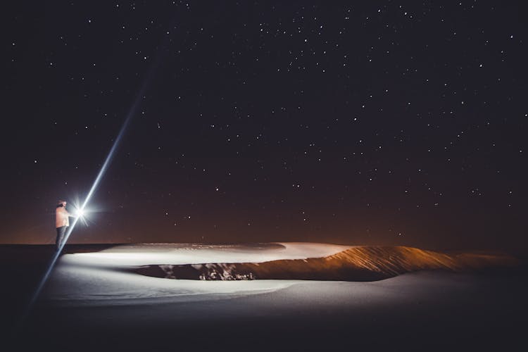 A Person With A Flashlight Under A Starry Night Sky