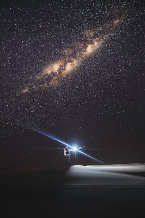 A Person with a Flashlight under a Starry Night Sky