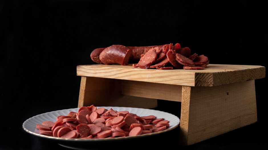 Sliced smoked sausage rounds with a browned, seared crust next to a whole uncut link on a wooden cutting board.