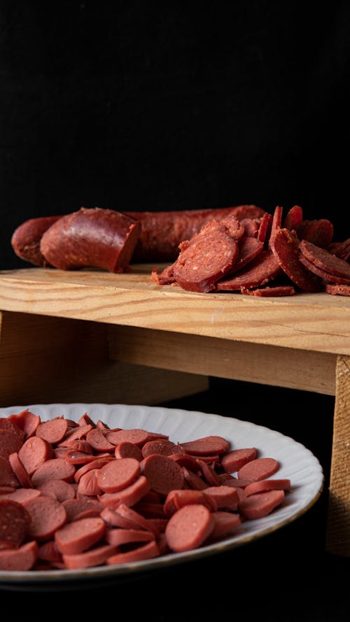 Free Bright yummy cut sausages on wooden cutting board and round shaped ceramic plate Stock Photo