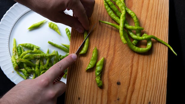 From above hands of crop unrecognizable person cutting hot peppers on cutting board and putting slices on plate