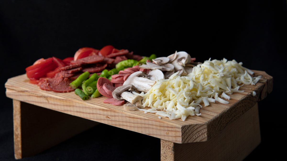 Queijos, calabresa e temperos frescos para pizza sobre tábua