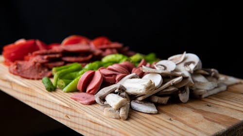 Selective focus of delicious meat sausages and mushrooms with vegetables on chopping board on black background
