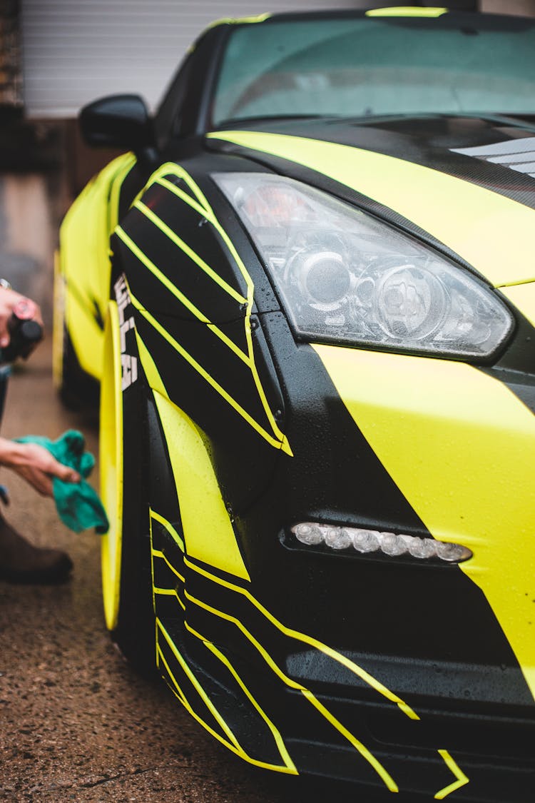 Crop Person Wiping Wheel Of Luxury Car