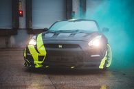 Contemporary sports car with headlights lights and yellow wrapping design parked near wall with closed blinds in green fume from smoke bomb
