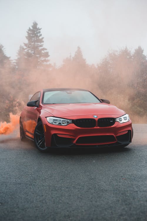 Bright modern car covered with colorful smoke on asphalt road against green trees