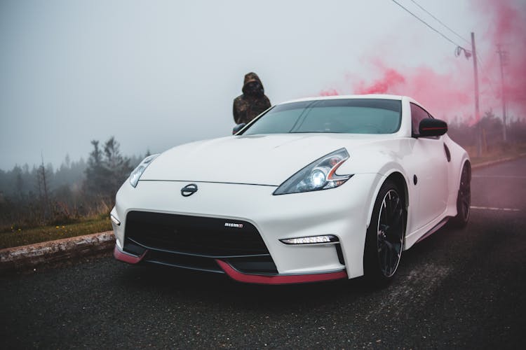 Person Standing Near Car With Stylish Headlights In Colored Smoke