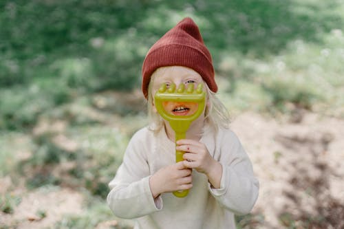 Cute little girl holding toy rake near face in garden