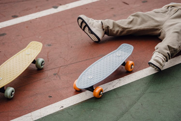 Crop Unrecognizable Kid Lying On Ground Near Skateboard