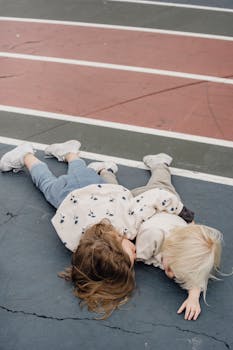 A serene moment of two children lying on a colorful sports track outdoors.