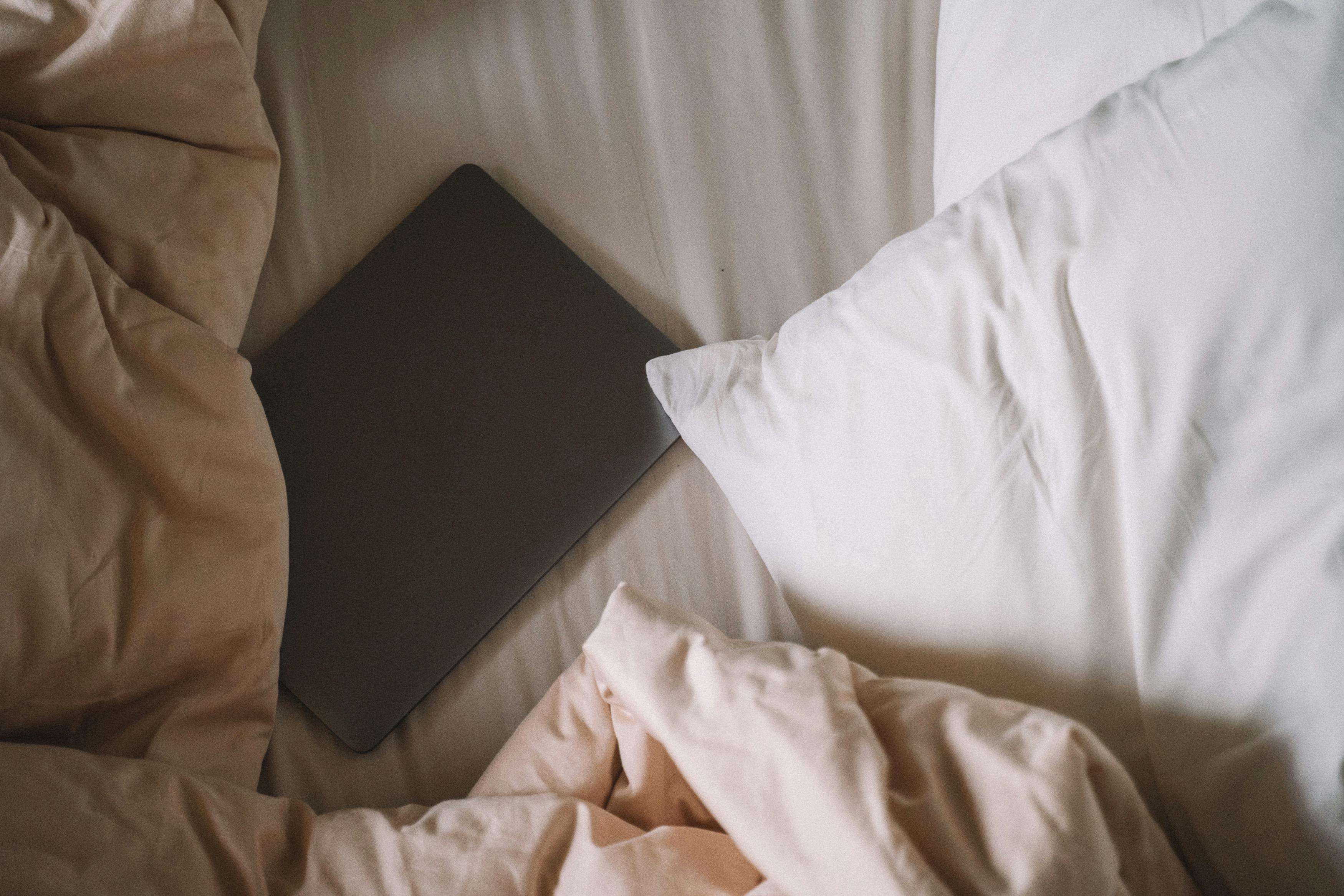 A laptop resting on an unmade bed with soft linens, offering a cozy and relaxed atmosphere.
