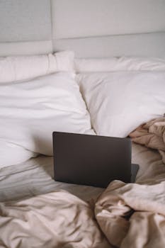A laptop rests on a cozy bed with pillows and blankets, ideal for relaxation or work-from-home.