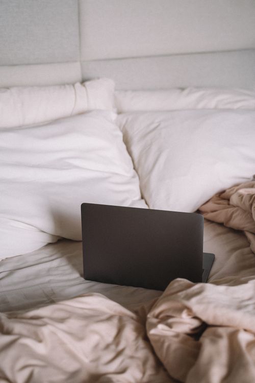 Free A laptop rests on a cozy bed with pillows and blankets, ideal for relaxation or work-from-home. Stock Photo