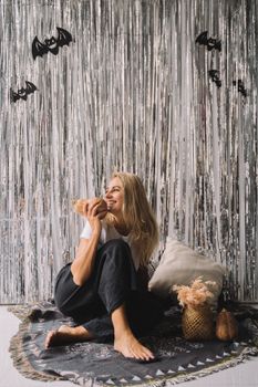 一位开朗的金发女人坐在万圣节装饰的房间里，微笑着