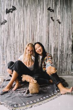 两个女人坐在装饰地毯上，在室内用南瓜庆祝万圣节
