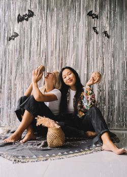 两个女人坐在室内，拿着椰子，享受着彼此的陪伴，周围装饰着万圣节的饰品