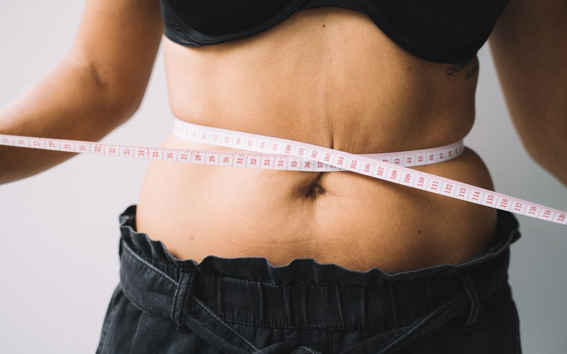 A person measuring their waist with a tape, symbolizing fitness and health goals.