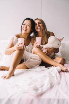 两个女人喝着饮料，抱着毛绒独角兽，享受着彼此的陪伴，洋溢着幸福