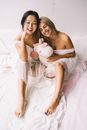 两个女人坐在床上，用毛绒独角兽玩具陪伴彼此