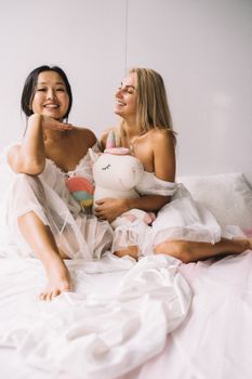 两个快乐的女人坐在床上，抱着毛绒玩具，一起享受这快乐的时光