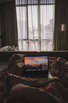 A laptop on a plush bed by the window in a cozy bedroom setting.
