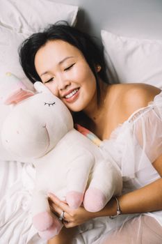 一位女士闭着眼睛，面带微笑，平静地抱着一个毛绒独角兽玩具，定格了这宁静的一刻