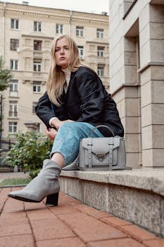 Stylish woman posing on a city sidewalk in trendy fall outfit with a fashionable bag.