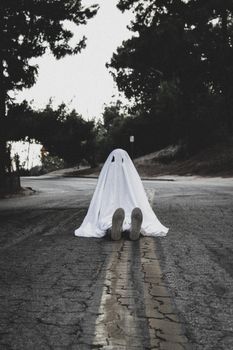 空旷的道路上，一个穿着幽灵服装的人坐着，唤起了万圣节的幽灵气氛