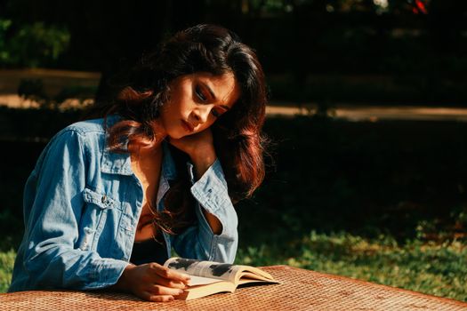 A young woman reading a book outdoors in a sunlit park, enjoying leisure time.
