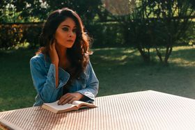 A contemplative woman in a denim jacket reading a book at an outdoor table, India.