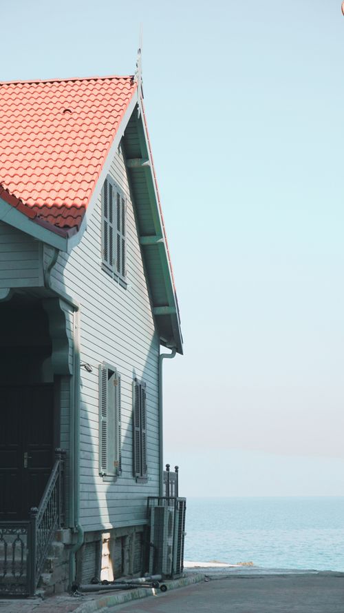 Free A serene view of a coastal house with a red roof overlooking the ocean under a clear sky. Stock Photo