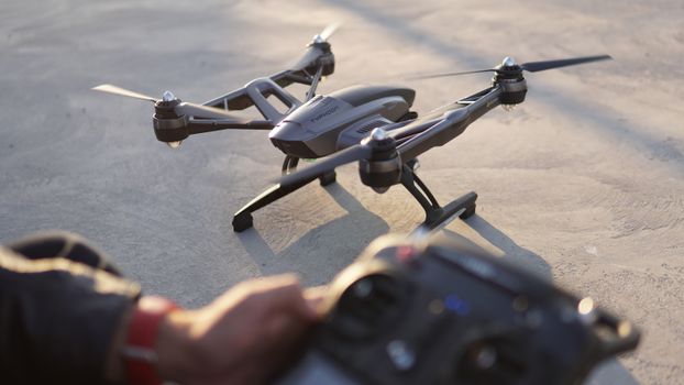 From above of quadcopter placed on asphalt pavement and crop anonymous drone operator with remote control at daytime