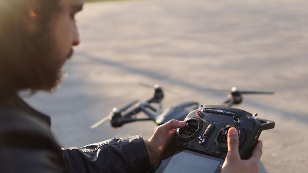 From above of crop bearded male operator controlling drone with remote control with display at daytime