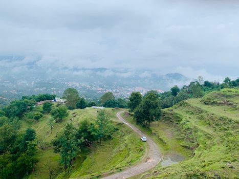 A breathtaking aerial view of Rawalakot, showcasing lush green hills and a winding dirt road under a cloudy sky.
