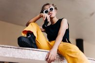 Woman in Black Tank Top and Yellow Skirt Sitting on Concrete Bench Using White Camera