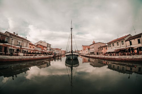 Exterior of small buildings near quiet water of canal with boat under cloudy gloomy sky