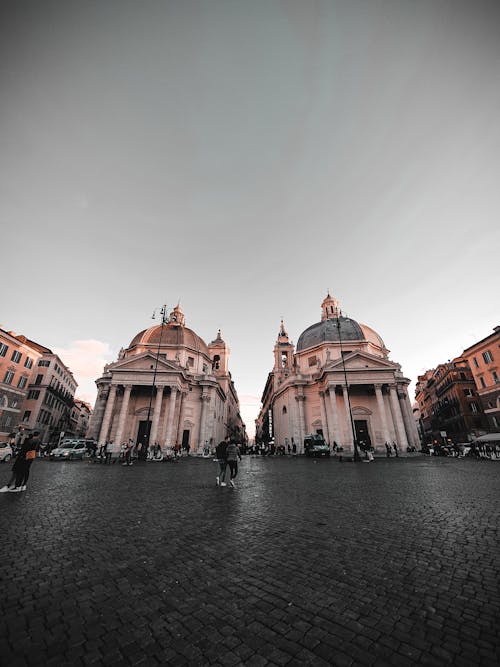 Low angle of tourist walking on square Piazza del Popolo with Santa Maria dei Miracoli and Santa Maria di Montesanto churches in Rome