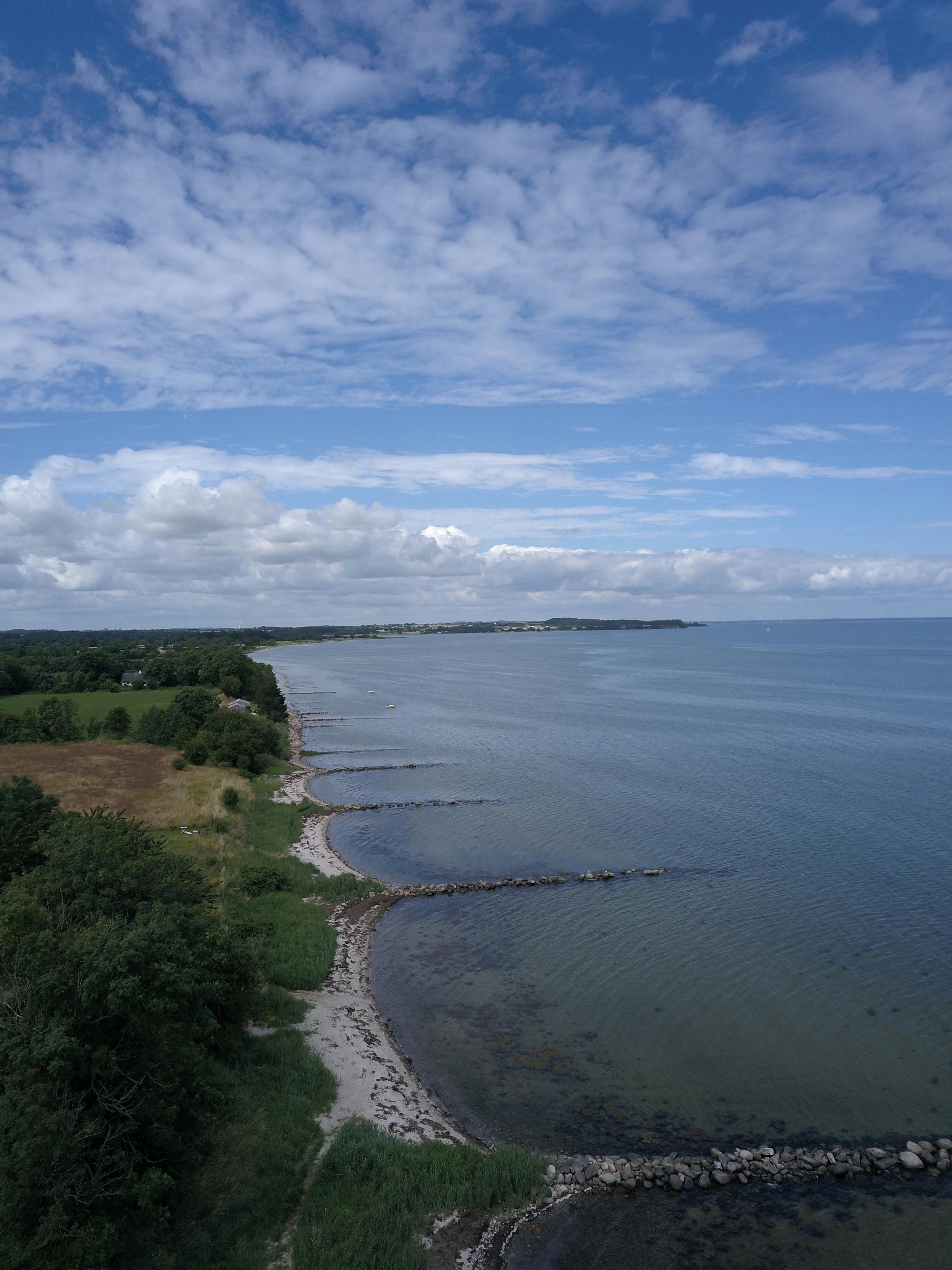 Aerial photo of the Danish coastline with lush greenery and clear blue seas on a bright day.