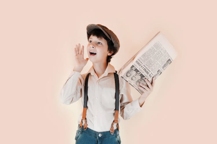 Cheerful Boy Holding Aged Newspaper Against Beige Background