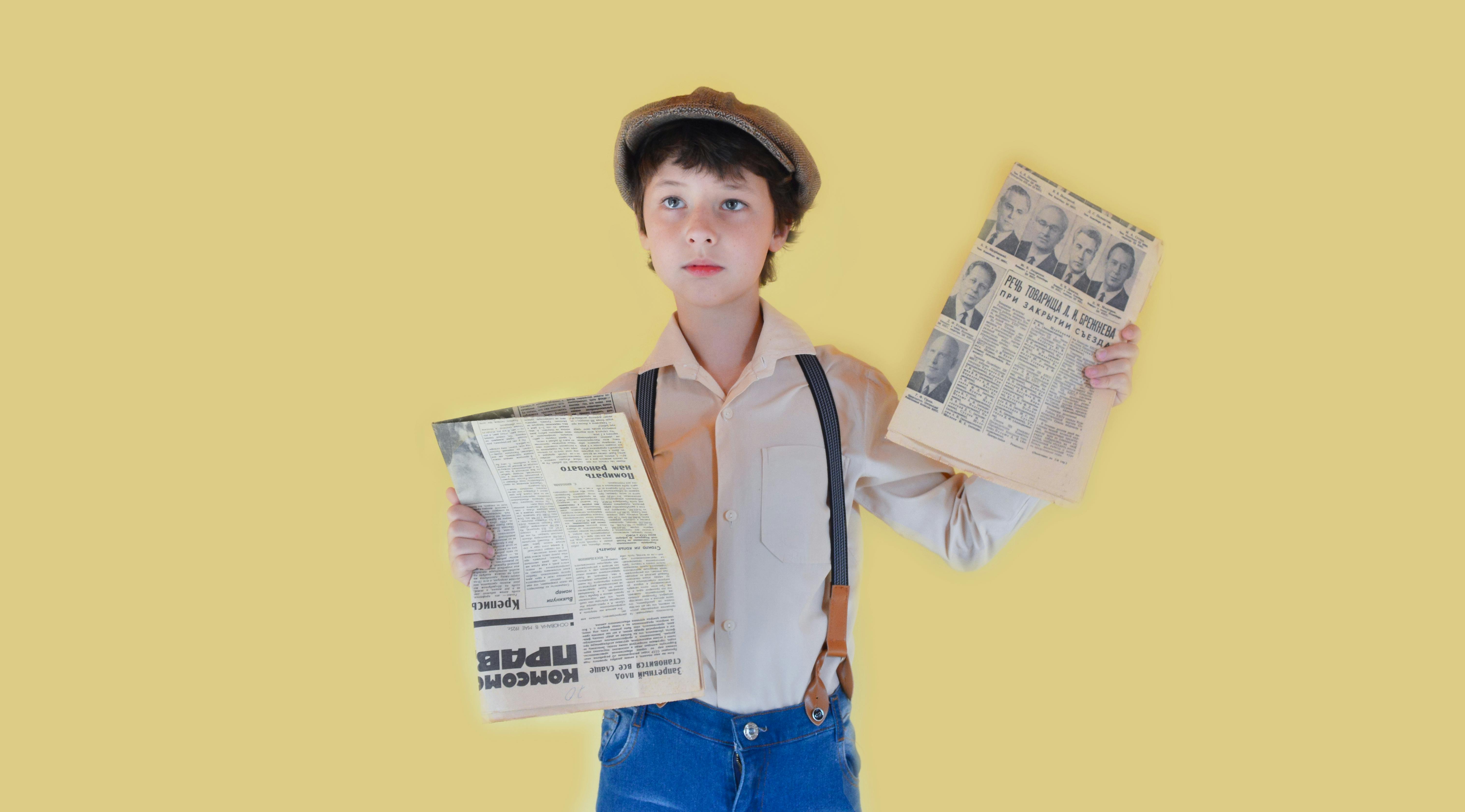 Pensive Boy Standing With Old Newspapers Against Yellow Background Free Stock Photo