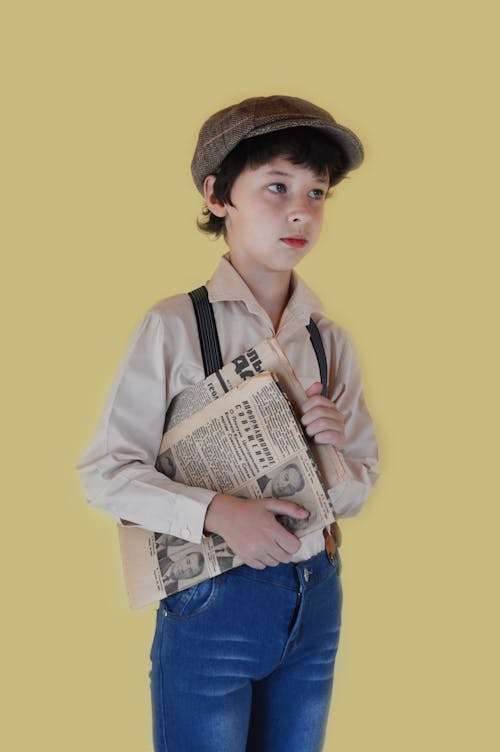 Thoughtful boy in stylish clothes standing with newspapers and looking away