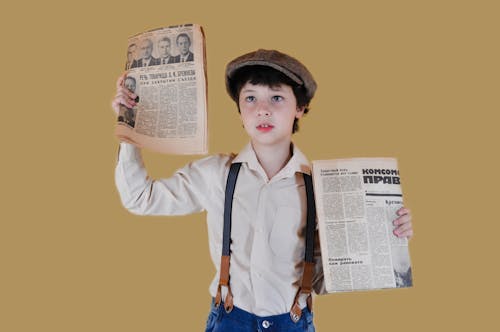 Stylish boy showing aged newspapers against yellow background