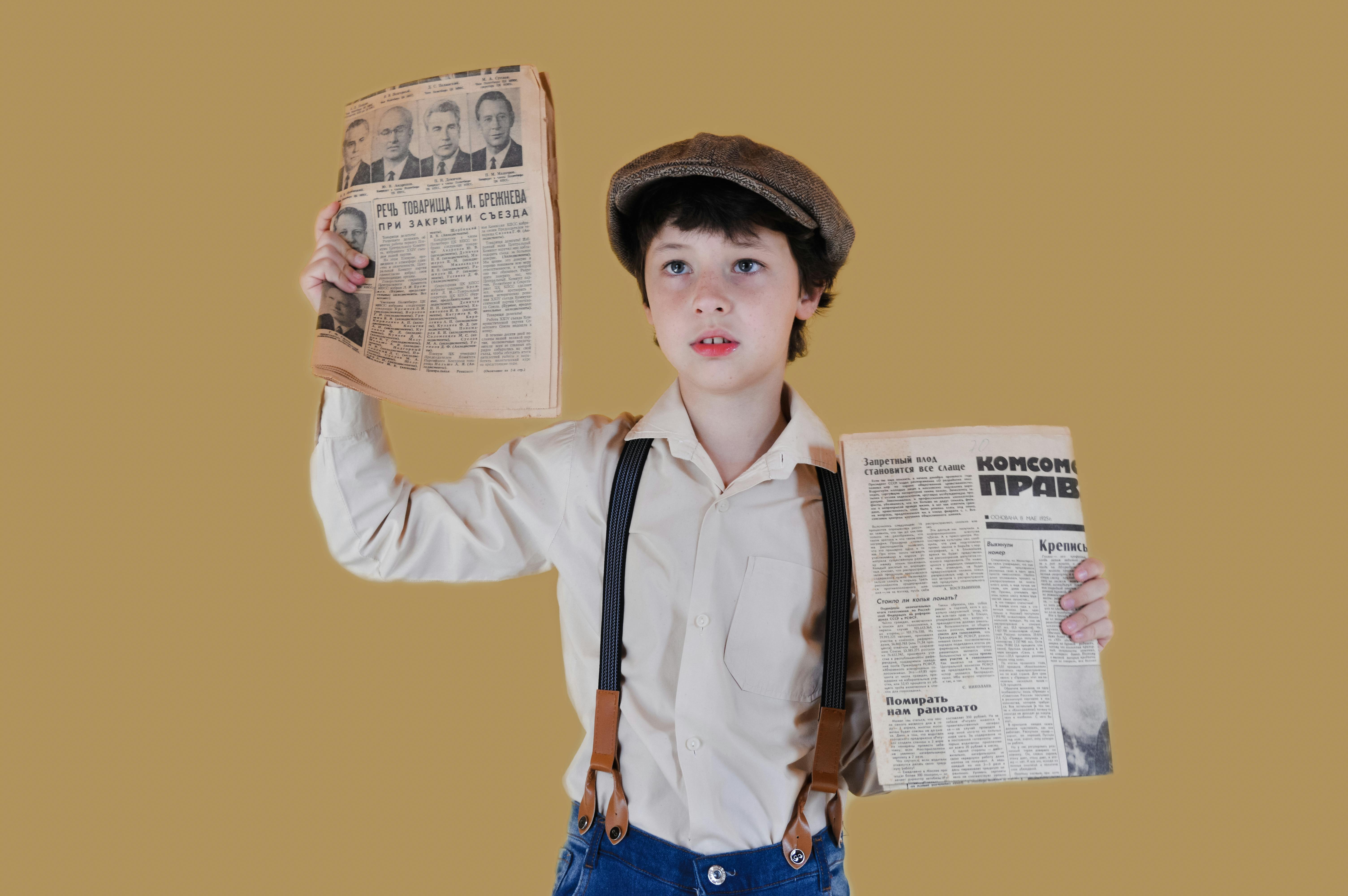 Stylish Boy Showing Aged Newspapers Against Yellow Background Free Stock Photo