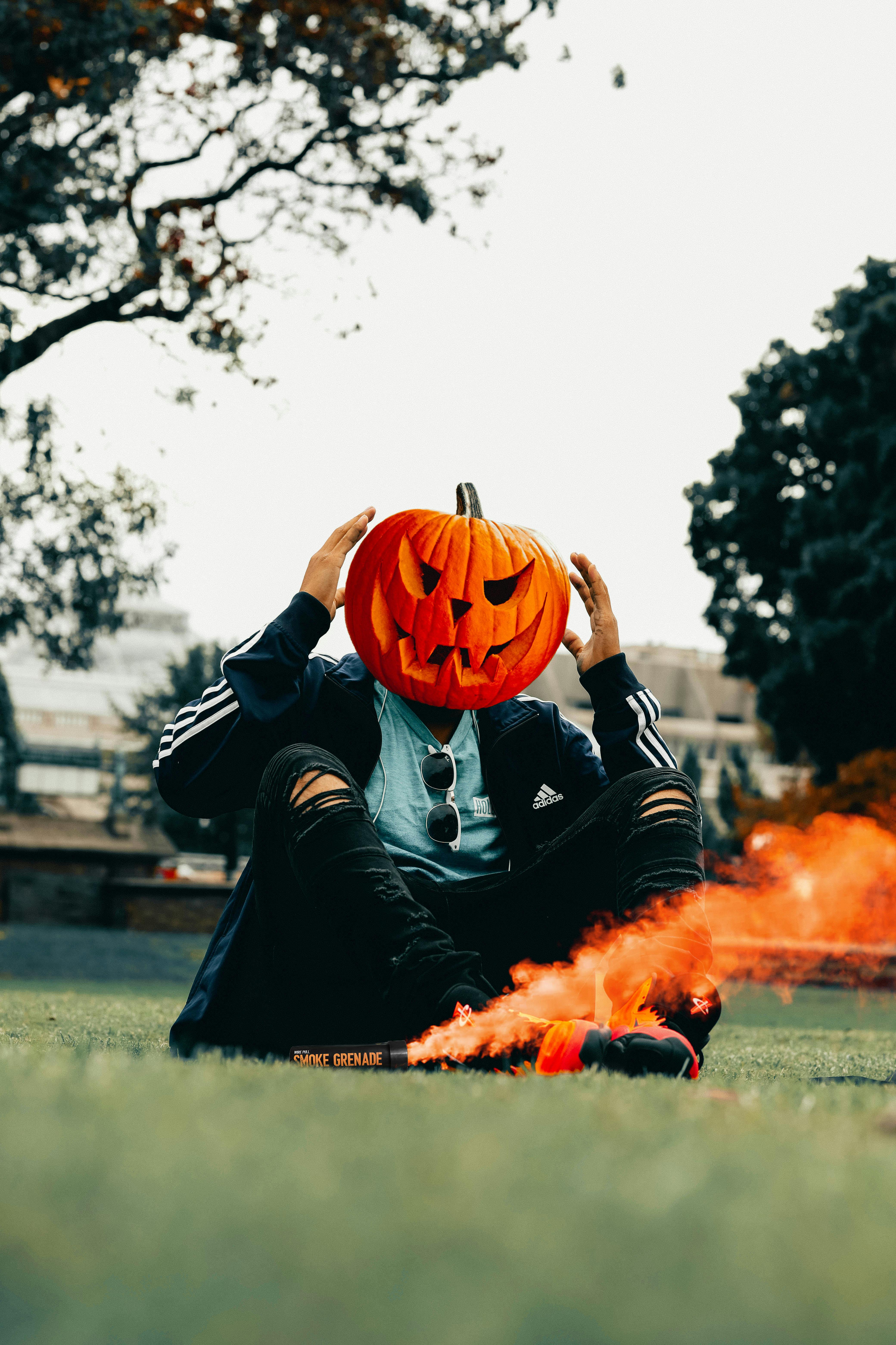 Person wearing a pumpkin head with flare in a park setting during fall.