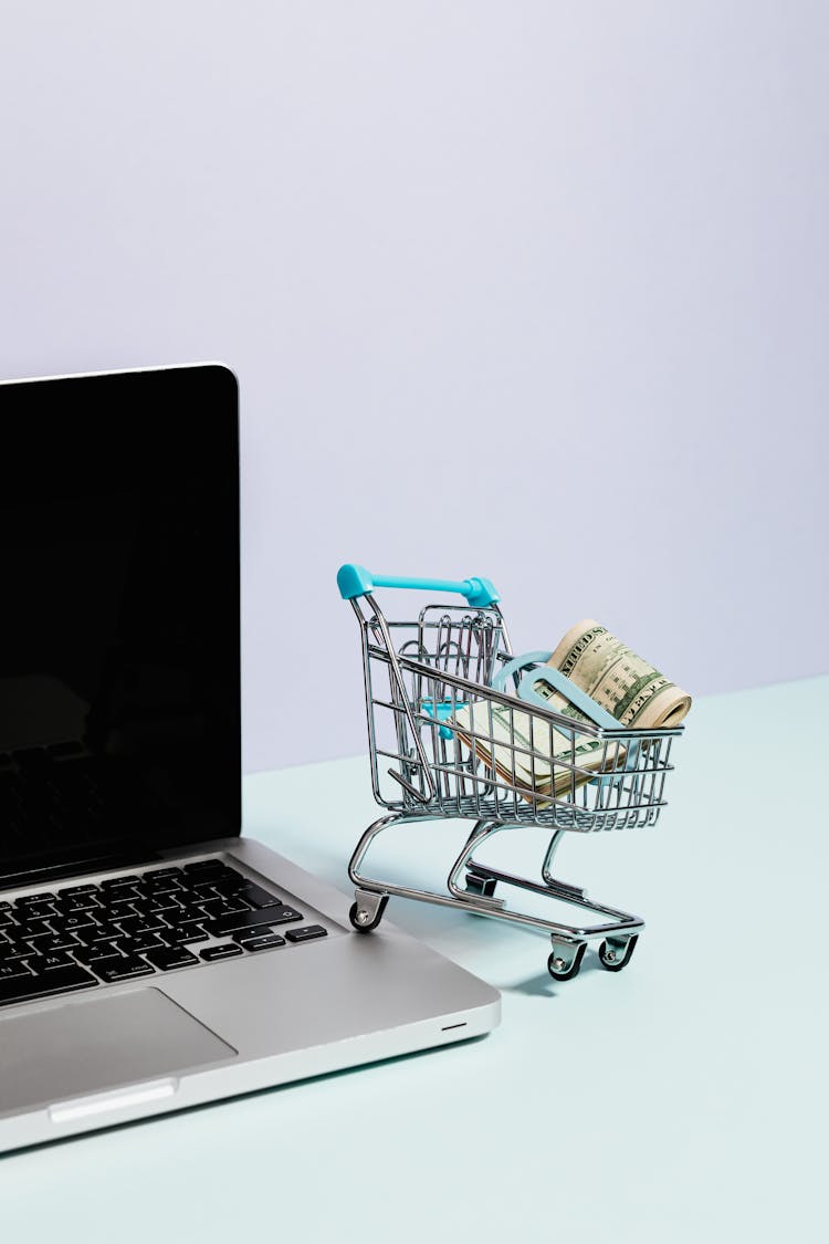 Shopping Cart With Money On Top Of A Laptop