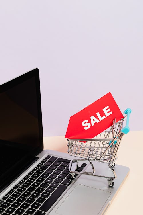 A Red Sale Tag on a Miniature Shopping Cart Placed on a Macbook Laptop